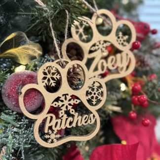 Two golden tree ornaments in an animal paw shape hanging in a christmas tree with a red flower in the right low corner.