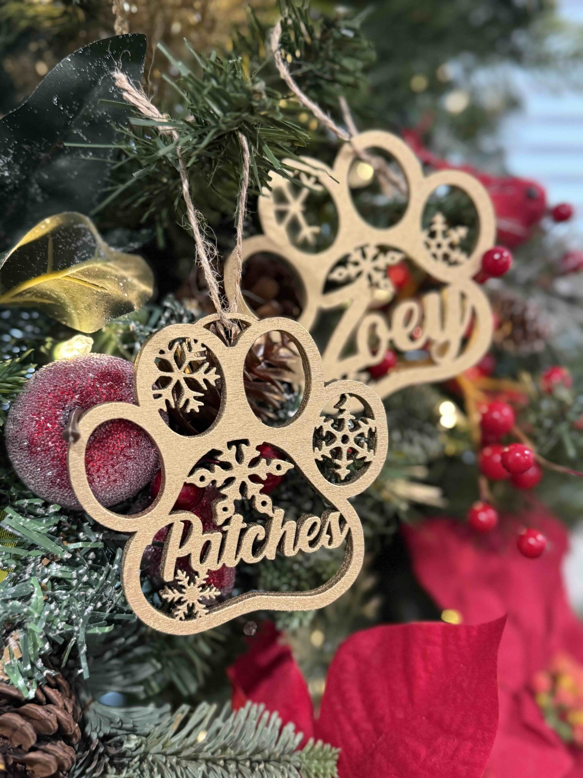 Two golden tree ornaments in an animal paw shape hanging in a christmas tree with a red flower in the right low corner.